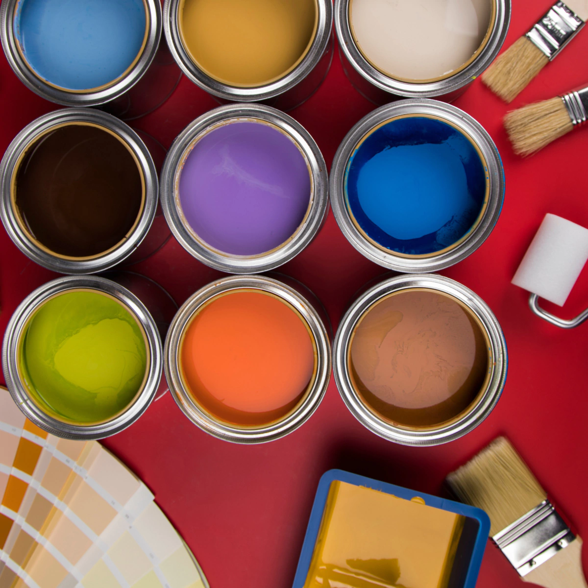 paint buckets and paint brushes laying a red surface